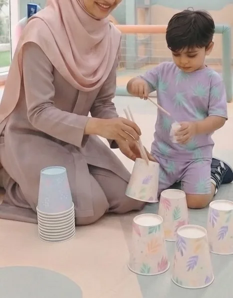 Illustration: an adult and a toddler sit face to face, playing with paper cups