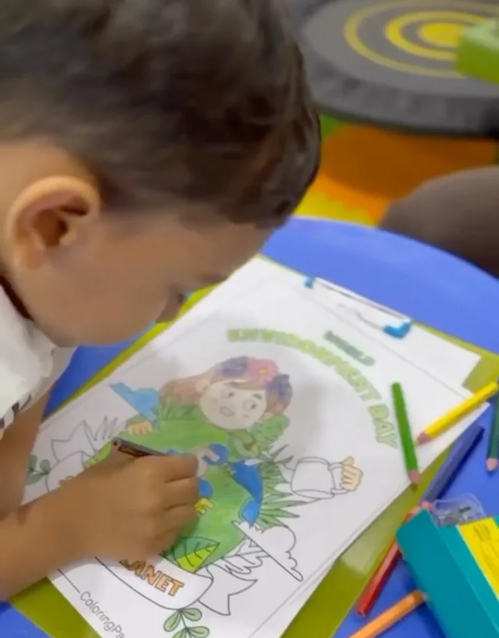 A child colours a worksheet with crayons at a table
